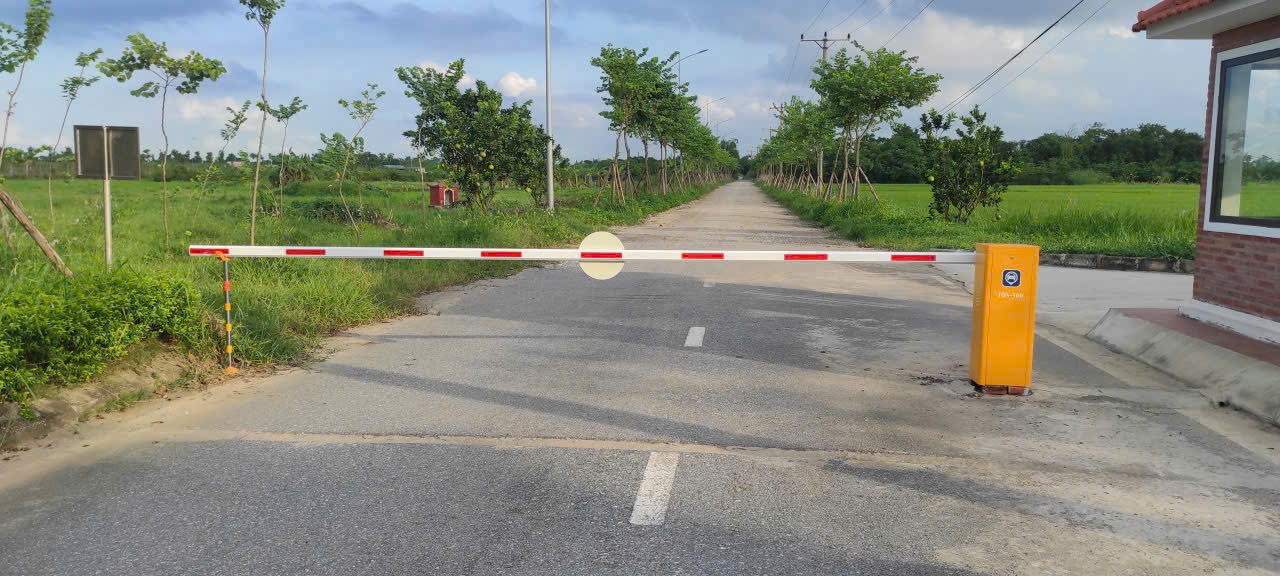Thanh chắn barie tự động màu trắng đỏ chặn lối vào con đường bê tông giữa cánh đồng xanh